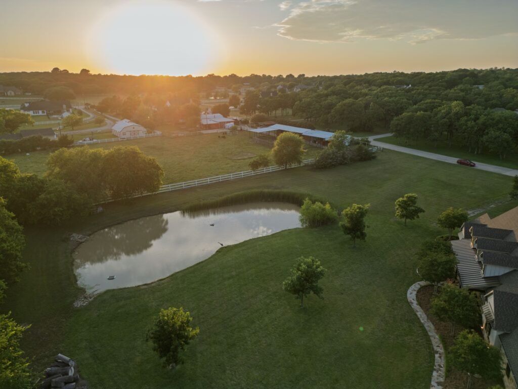 Aerial view at sunset of an acreage property with a pond and pasture in Keller, TX 76262